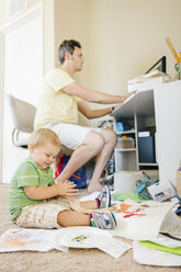 Vater arbeitet am Computer, während sein kleiner Sohn auf dem Boden spielt - ISF02371