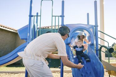 Familie auf dem Spielplatz, kleiner Sohn rutscht die Rutsche hinunter - ISF02385