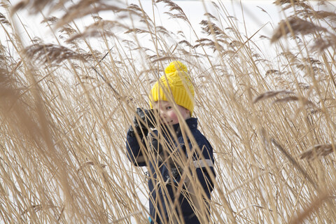 Junge im langen Gras stehend, in schneebedeckter Landschaft, lizenzfreies Stockfoto