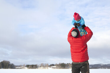 Father lifting young son in air, in snow covered landscape - ISF02411