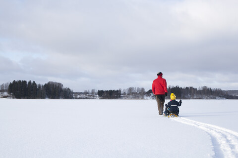 Vater, der seine Söhne auf einem Schlitten durch eine verschneite Landschaft zieht, Rückansicht, lizenzfreies Stockfoto