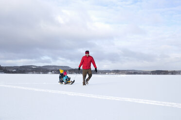 Father pulling sons along on sledge in snow covered landscape - ISF02414