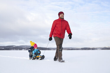 Father pulling sons along on sledge in snow covered landscape - ISF02415
