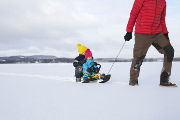 Vater, der seine Söhne auf einem Schlitten durch eine verschneite Landschaft zieht, tiefer Ausschnitt - ISF02416