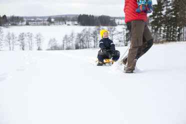 Vater, der seinen Sohn auf einem Schlitten zieht und den Jungen auf dem Arm trägt, in einer verschneiten Landschaft, tiefer Ausschnitt - ISF02420