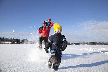 Vater und zwei Söhne, die durch eine schneebedeckte Landschaft rennen - ISF02426