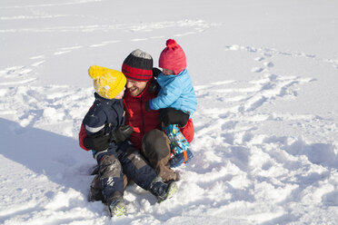 Vater sitzt im Schnee und umarmt zwei Söhne - ISF02432