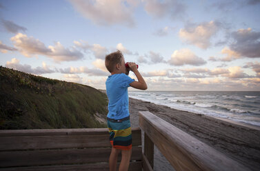 Junge am Strand, der die Aussicht durch ein Fernglas betrachtet, Blowing Rocks Preserve, Jupiter, Florida, USA - ISF02471