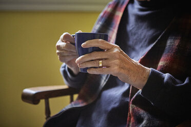 Ältere Frau auf einem Stuhl sitzend, heißes Getränk in der Hand, Mittelteil - ISF02477
