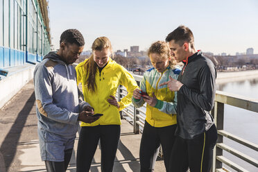 Sportliche Freunde prüfen auf einer Brücke in der Stadt ihre Handys - WPEF00313