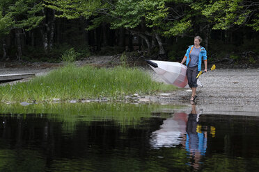 Kayaker carrying kayak to water edge, Kejimkujik Lake, Nova Scotia, Canada - ISF02509