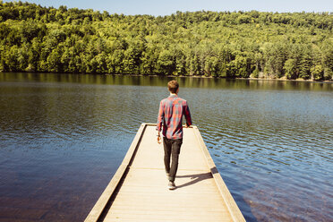 Mann geht entlang eines Holzstegs am See, Rückansicht - ISF02514