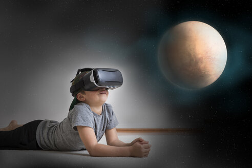 Young boy lying on floor, wearing virtual reality headset, looking at planet, digital composite - ISF02518