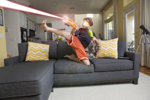 Junge auf Sofa, trägt Virtual-Reality-Headset, tritt Bein, feuert Laserwaffen, digitales Komposit - ISF02523