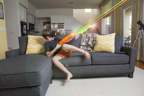 Young boy on sofa, wearing virtual reality headset, firing laser guns, digital composite stock photo