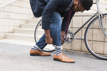 Junger männlicher Radfahrer rollt Jeans auf dem Bahnsteig herunter - ISF02535