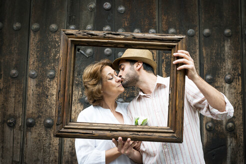 Portrait of adult son kissing mother on cheek, holding wooden frame in front of their faces, Mexico City, Mexico - ISF02561