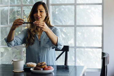 Young woman photographing doughnut holes on table - ISF02582