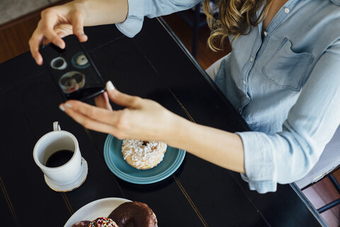 Draufsicht auf eine Frau, die ein Donut-Loch und Kaffee auf einem Tisch fotografiert, lizenzfreies Stockfoto