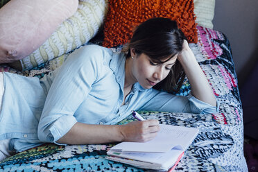 Young woman lying on shabby chic bed writing in notebook - ISF02587