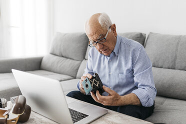 Ein älterer Mann benutzt einen Laptop und hält seine alte Fotokamera - JRFF01665