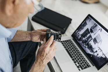 Älterer Mann, der einen Laptop benutzt und seine alte Fotokamera hält, Bildschirm mit altem Foto - JRFF01667