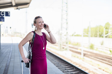 Lächelnde reife Frau am Telefon wartet am Bahnsteig - DIGF04469