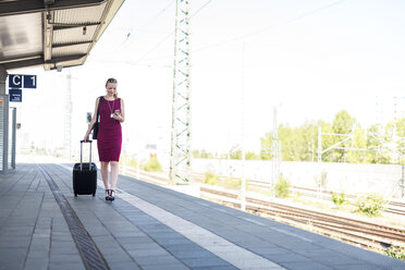 Ältere Geschäftsfrau mit Smartphone und Koffer auf dem Bahnsteig - DIGF04470