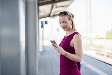 Lächelnde reife Frau steht auf dem Bahnsteig und schaut auf ihr Handy - DIGF04472