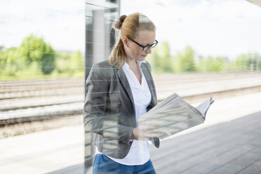 Ältere Geschäftsfrau wartet am Bahnsteig und liest Zeitung - DIGF04478