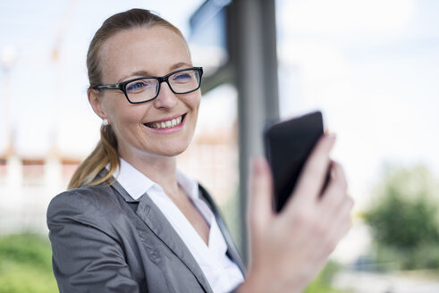 Porträt einer lächelnden Geschäftsfrau, die auf ihr Mobiltelefon schaut - DIGF04486