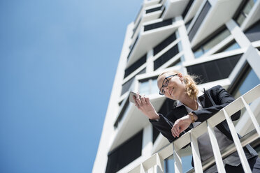Porträt einer Geschäftsfrau, die auf einem Balkon steht und ein Mobiltelefon benutzt - DIGF04487