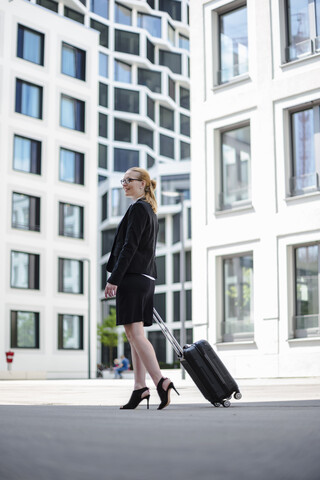 Reife Geschäftsfrau mit Koffer, die vor einem Bürogebäude spazieren geht, lizenzfreies Stockfoto
