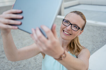 Portrait of smiling woman wearing glasses taking selfie with tablet - DIGF04497