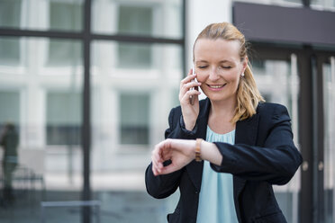 Porträt einer lächelnden Geschäftsfrau, die am Telefon die Zeit überprüft - DIGF04500