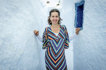 Woman standing in narrow gap between walls, Oía, Santorini, Kikladhes, Greece - ISF02631