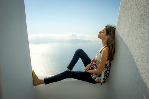 Mädchen sitzend, an die Wand gelehnt, Meer im Hintergrund, Oía, Santorin, Kikladhes, Griechenland - ISF02635