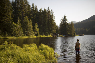 Teenage boy standing in lake, rear view - ISF02639