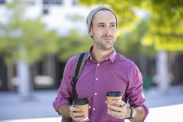 Junger Mann im Freien, zwei Kaffeebecher zum Mitnehmen in der Hand - ISF02761