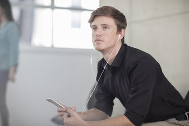 Junger männlicher Büroangestellter träumt am Schreibtisch und hört Kopfhörer - ISF02779