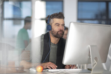 Man in office wearing headphones, using computer - ISF02787