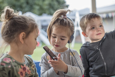 Junges Mädchen mit Freunden, die ein Smartphone benutzen und Kopfhörer tragen - ISF02791