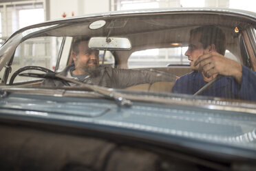 Zwei Automechaniker unterhalten sich auf dem Vordersitz eines Oldtimers in einer Reparaturwerkstatt - ISF02817