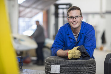 Porträt eines männlichen Automechanikers, der sich in einer Reparaturwerkstatt an die Reifen lehnt - ISF02845