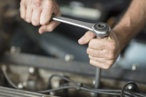 Hände eines männlichen Automechanikers, der einen Schraubenschlüssel in einer Reparaturwerkstatt benutzt, lizenzfreies Stockfoto