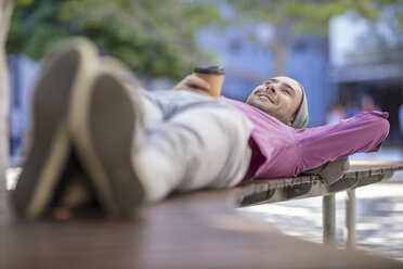 Junger Mann im Freien, auf einer Bank liegend, mit einem Kaffeebecher zum Mitnehmen - ISF02862