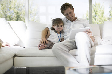 Father using digital tablet with baby girl on sofa - ISF02876