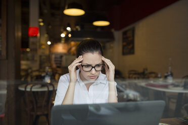 Woman in coffee shop using laptop looking stressed - ISF02914