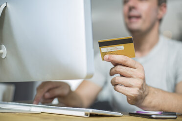 Abgeschnittene Ansicht eines Mannes, der eine Kreditkarte hält und einen Computer benutzt - ISF02920
