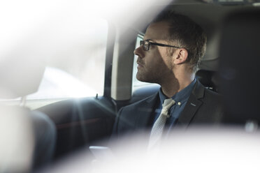 Businessman sitting in back of car, holding smartphone - ISF02944